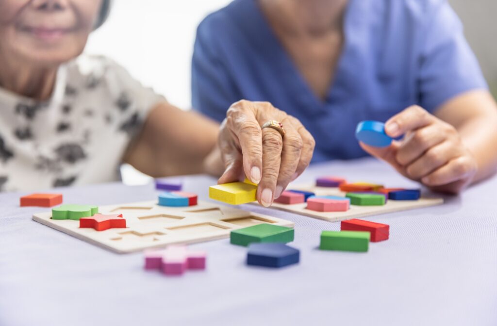 A staff member helps an older adult complete a wooden shape puzzle in memory care.