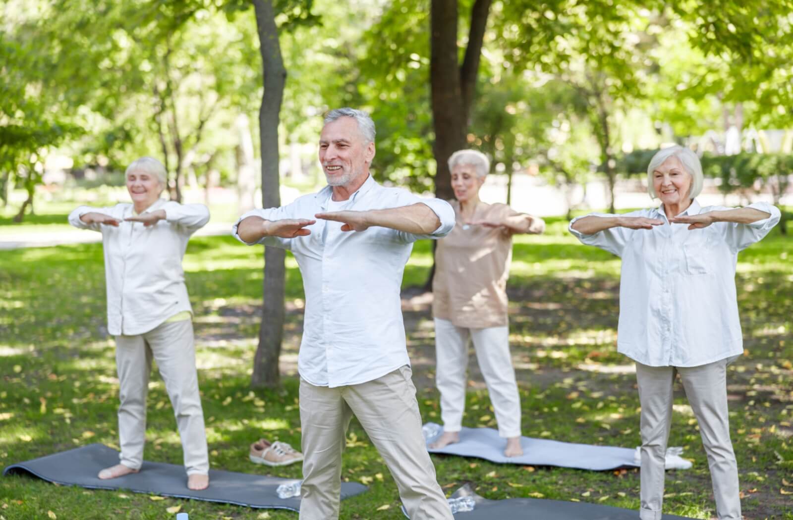 A group of smiling seniors practices a relaxing Tai Chi flow in a local green space.