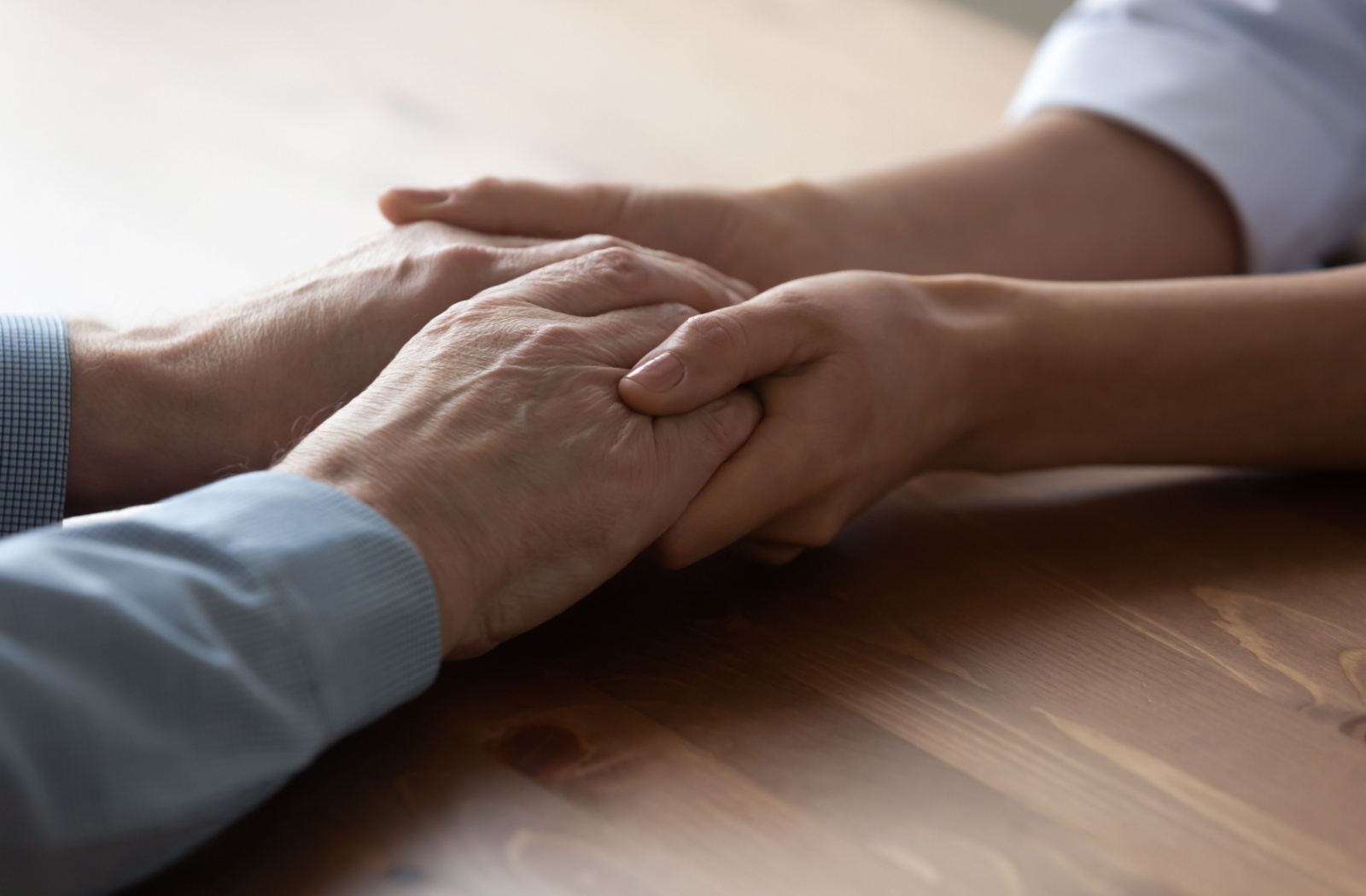 A close-up image of an adult child clasping their parent's hands while discussing a move to assisted living.