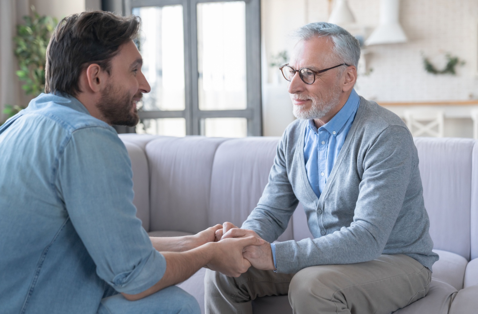 An adult child sitting across from their smiling older parent, discussing a potential move to assisted living.
