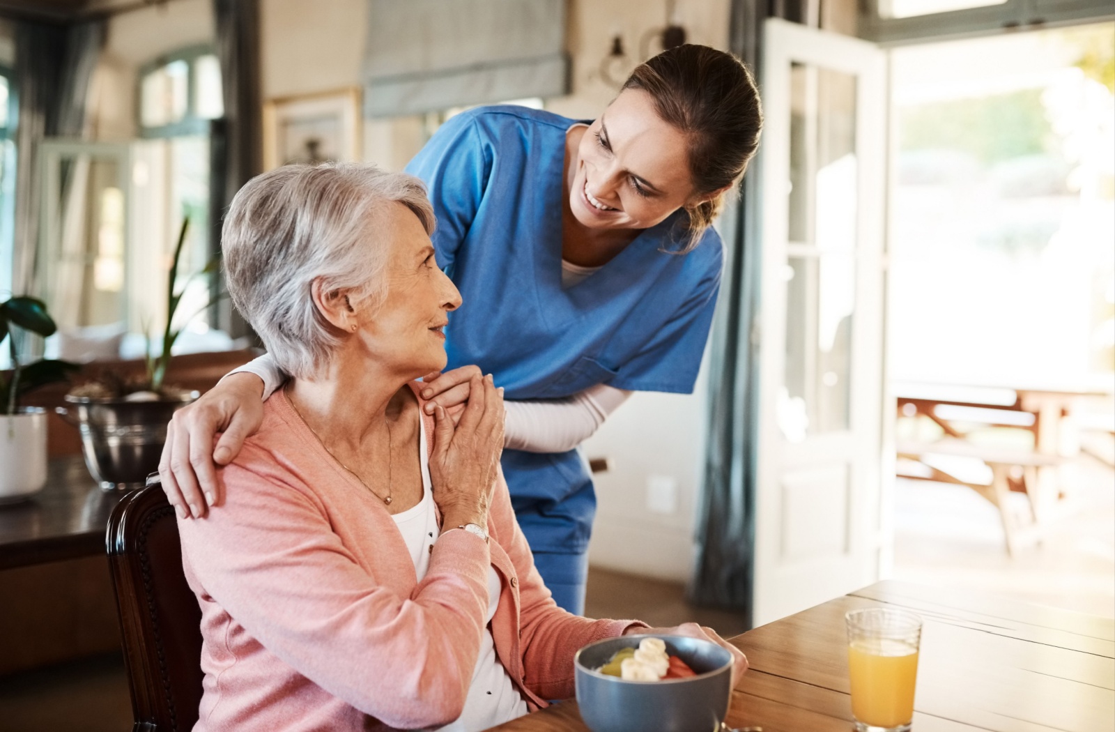 A caregiver checking in on a happy resident in personal care during breakfast.
