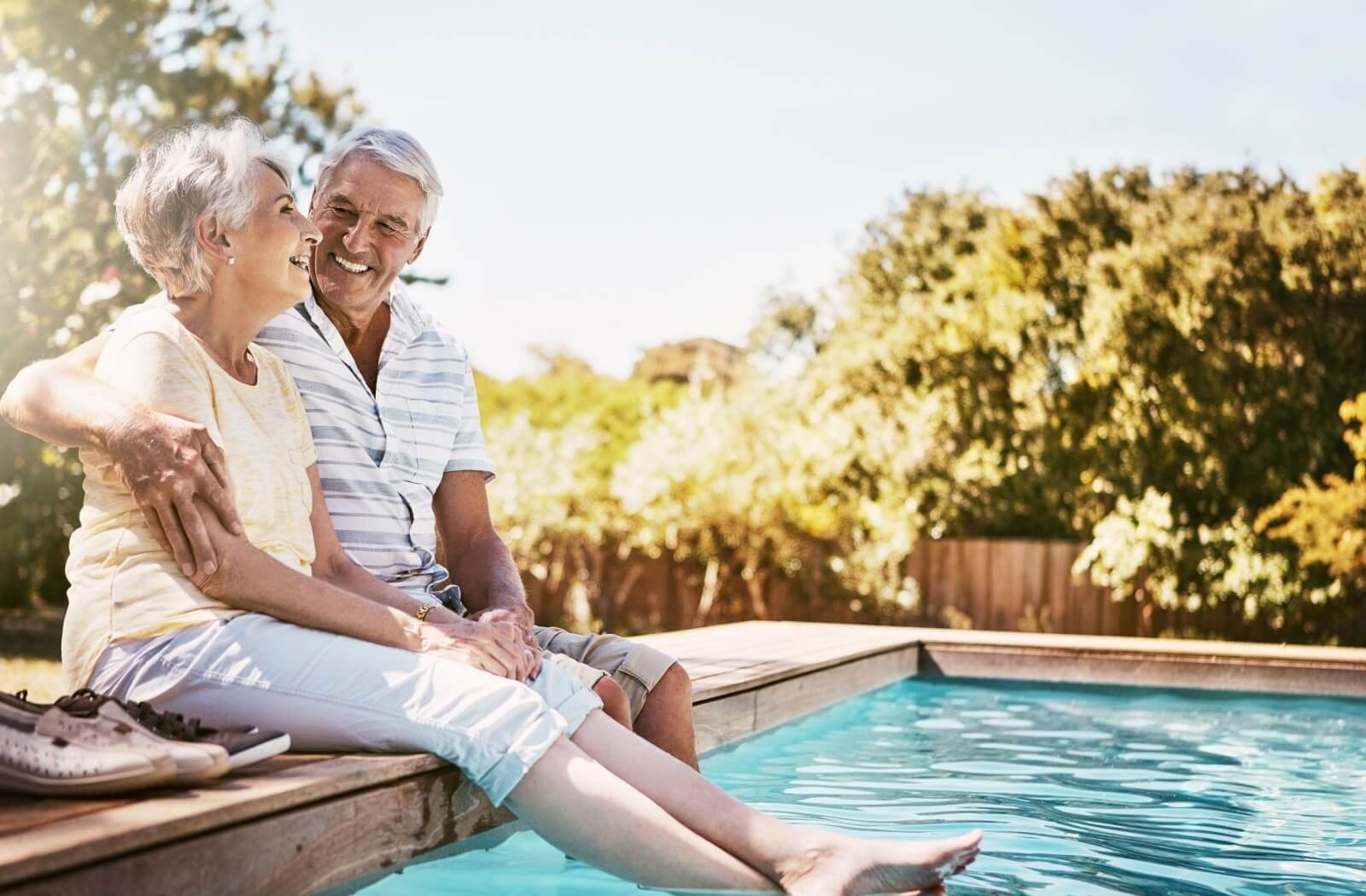 An older couple relaxes poolside on a sunny summer day, dipping their toes into the water.