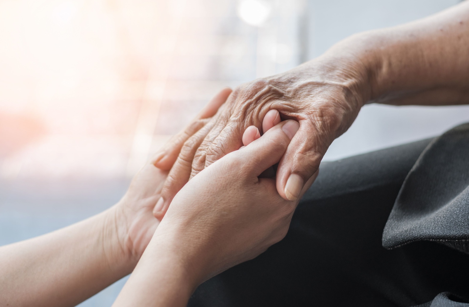 A close-up of a staff member's hand holding an older adult's hand in assisted living.