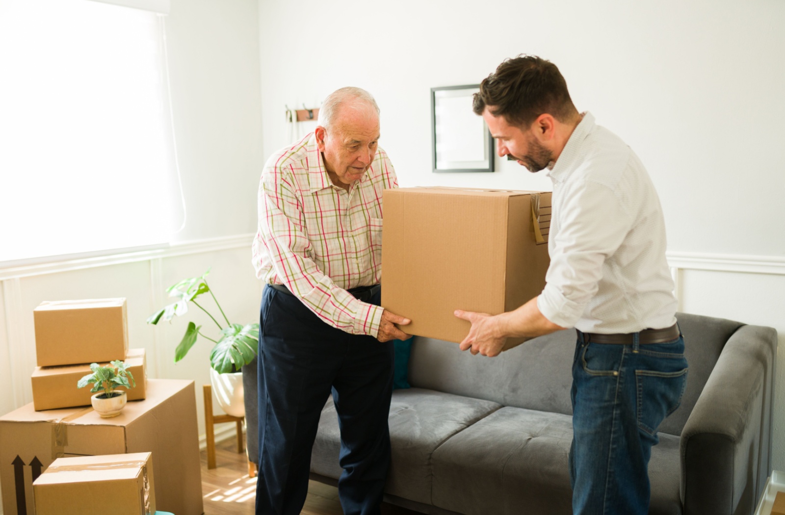 A senior is being helped by a young adult to carry a cardboard box.