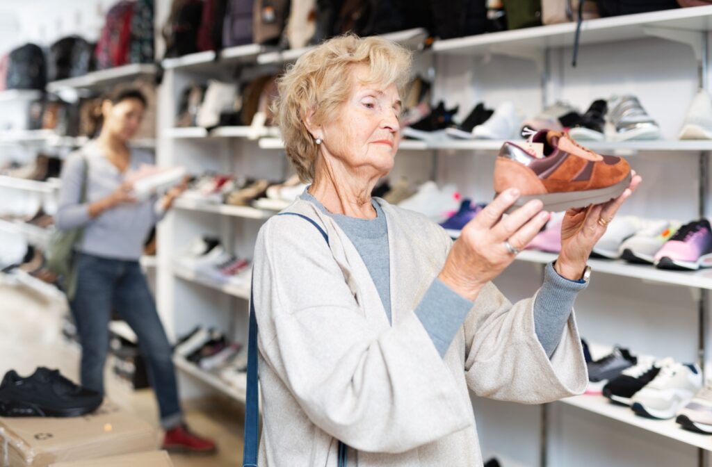 An older adult in a shoe store looks at a shoe while holding it in with both hands.