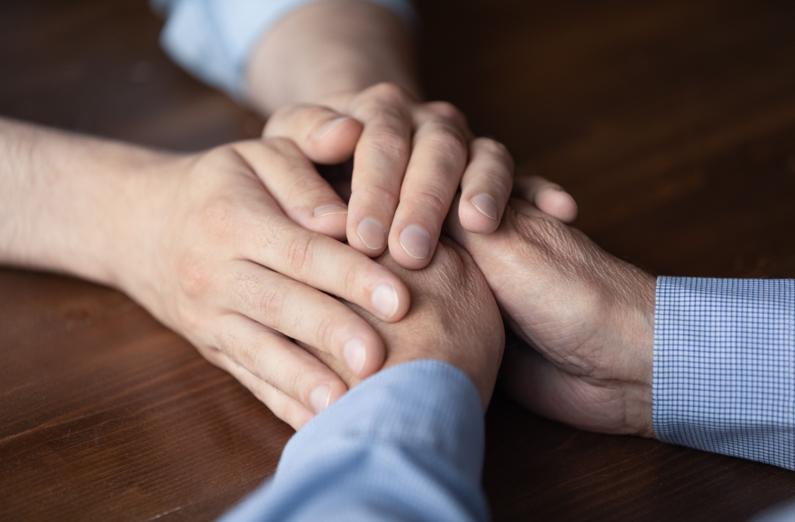 A close-up image of an adult clasping the hands of their parent with dementia.