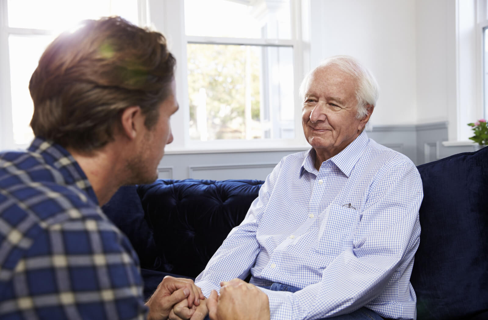 An older adult with dementia smiling while holding the hand of their adult child during a conversation.